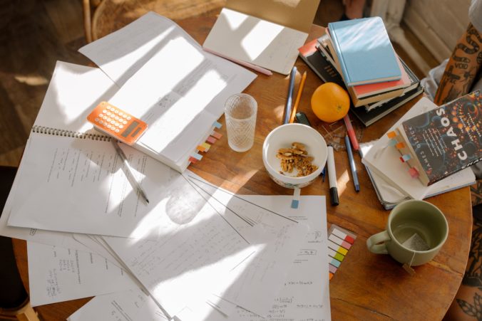 Foto eines Arbeitsplatzes mit Büchern und vielen beschriebenen Zetteln die durcheinander auf dem Tisch liegen.
